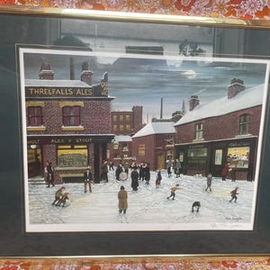 May include: A framed print depicting a snowy town scene with brick buildings, including a pub labeled Threlfalls Ales and a fish and chips shop. People are walking through the snow-covered street under a dark sky with a visible moon.