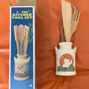 Puede incluir: Un juego de 5 utensilios de cocina con un soporte de cerámica con un diseño de gallina. El juego incluye cucharas de madera, un batidor y un tenedor. La caja dice "5 PCS KITCHEN TOOL SET". El soporte mide aproximadamente 15 cm de alto.