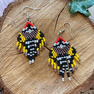May include: A pair of beaded earrings with a geometric pattern in black, white, yellow, and red. The earrings have a fringe of beads at the bottom.