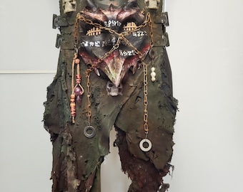 Op de afbeelding: Een handgemaakt, verweerd leren borststuk met een demonisch gezichtsontwerp. Het borststuk heeft een donkergroen en bruin kleurenschema, met schedelaccenten, kettingen en bungelende ornamenten. Het ontwerp bevat hoorns en een oud schrift.