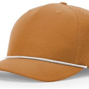 May include: A tan baseball cap with a curved brim and a white rope detail. The cap has a perforated side panel for ventilation. The hat is a solid color and has a classic, sporty design.