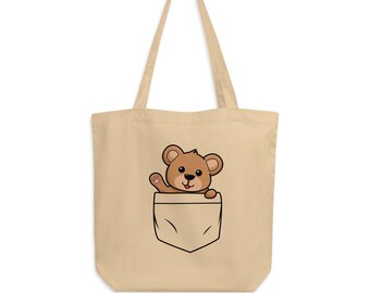 May include: A beige canvas tote bag with a brown teddy bear peeking out of a front pocket. The teddy bear is waving with its right paw.