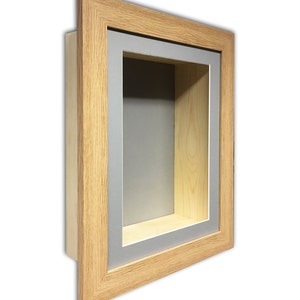 May include: A wooden shadow box with a light brown frame and a grey interior. The box has a rectangular opening and a recessed interior, ideal for displaying small items or artwork. The frame is made of natural wood.