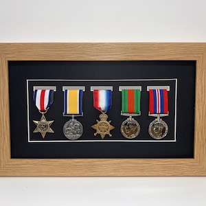 May include: A framed display of six medals with black matting and a light wood frame. The medals are arranged in a row with ribbons.
