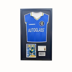 May include: A framed blue Chelsea Football Club jersey with the Umbro logo and Autoglass sponsor. The jersey is displayed with a Chelsea matchday programme and a ticket stub.