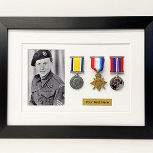K&ouml;nnte beinhalten: Ein schwarzer gerahmter Bilderrahmen mit einem Schwarzwei&szlig;foto eines Mannes in Milit&auml;runiform. Das Foto ist von drei Medaillen mit B&auml;ndern umgeben. Der Text "Your Text Here" ist auf einer goldenen Plakette unter den Medaillen gedruckt.