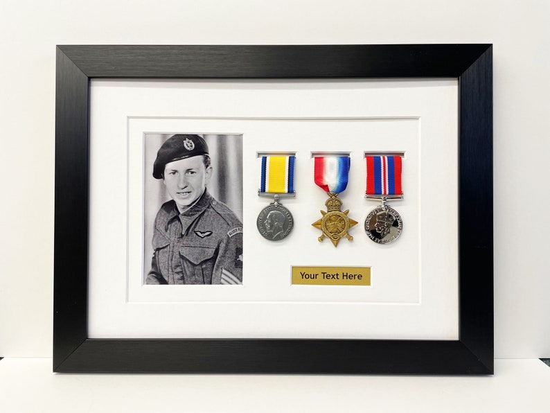 K&ouml;nnte beinhalten: Ein schwarzer gerahmter Bilderrahmen mit einem Schwarzwei&szlig;foto eines Mannes in Milit&auml;runiform. Das Foto ist von drei Medaillen mit B&auml;ndern umgeben. Der Text "Your Text Here" ist auf einer goldenen Plakette unter den Medaillen gedruckt.
