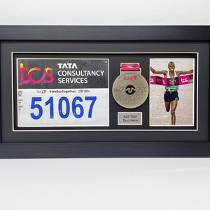 May include: A black framed display with a white background. The display features a silver medal with the text "TCS 2023" and a runner crossing the finish line. The display also includes a race bib with the text "TATA CONSULTANCY SERVICES" and the number "51067".