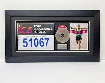 May include: A black framed display with a white background. The display features a silver medal with the text "TCS 2023" and a runner crossing the finish line. The display also includes a race bib with the text "TATA CONSULTANCY SERVICES" and the number "51067".