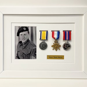 K&ouml;nnte beinhalten: Ein wei&szlig;er Rahmen mit einem Schwarzwei&szlig;foto eines Mannes in Milit&auml;runiform. Der Rahmen enth&auml;lt au&szlig;erdem drei Medaillen mit B&auml;ndern, eine kleine Plakette mit dem Text "Your Text Here" und eine kleine runde Medaille.
