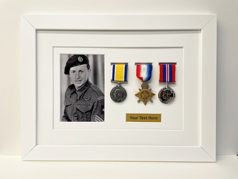 K&ouml;nnte beinhalten: Ein wei&szlig;er Rahmen mit einem Schwarzwei&szlig;foto eines Mannes in Milit&auml;runiform. Der Rahmen enth&auml;lt au&szlig;erdem drei Medaillen mit B&auml;ndern, eine kleine Plakette mit dem Text "Your Text Here" und eine kleine runde Medaille.