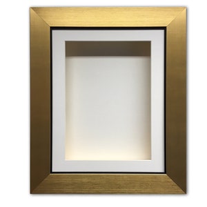 May include: A gold-coloured shadow box frame with a white interior and a black border. The frame is rectangular and has a textured surface, ideal for displaying artwork or memorabilia.
