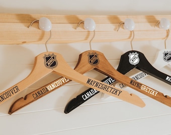 May include: Four wooden hangers with NHL logos and personalized text. The hangers are in different colors: brown, black, and white. The text on the hangers reads "Canada Vancouver", "Wayne Gretzky", and "Wayne Gretzky".