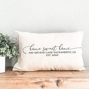 May include: A white throw pillow with the text "home sweet home" in black cursive script. Below the text is the address "430 Sievens Lane Sacramento, CA EST. 2020" in black.