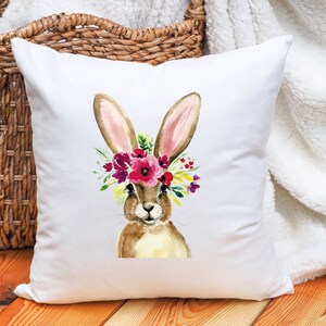 May include: White pillow with a watercolor illustration of a brown bunny wearing a pink and purple flower crown.