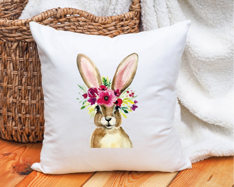 May include: White pillow with a watercolor illustration of a brown bunny wearing a pink and purple flower crown.