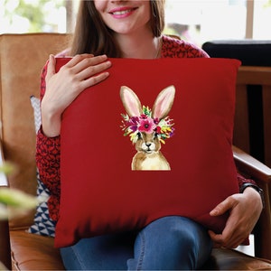 May include: Red throw pillow with a watercolor illustration of a brown bunny wearing a flower crown. The bunny has pink ears and a white nose.