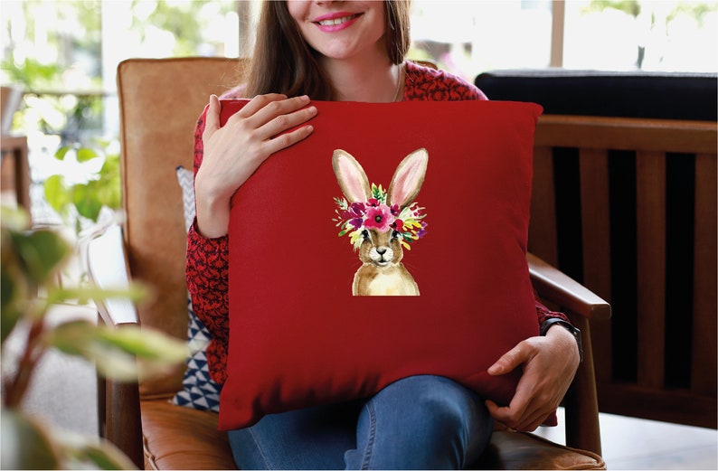 May include: Red throw pillow with a watercolor illustration of a brown bunny wearing a flower crown. The bunny has pink ears and a white nose.