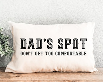 May include: White throw pillow with black text that reads "DAD'S SPOT DON'T GET TOO COMFORTABLE".