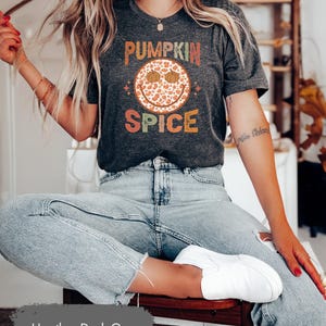 May include: A heather dark grey t-shirt with a smiling pumpkin face graphic and the text "Pumpkin Spice" in a retro font.