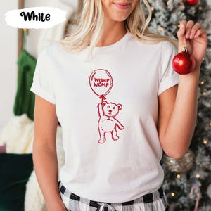 Puede incluir: Camiseta blanca con un oso de dibujos animados rojo sosteniendo un globo rojo que dice "Womp Womp".