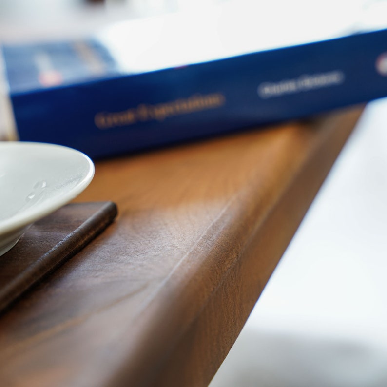 Op de afbeelding: Een close-up van een houten tafel met een wit bord en een blauw boek erop. De tafel heeft een natuurlijke houtnerf en een glad oppervlak.