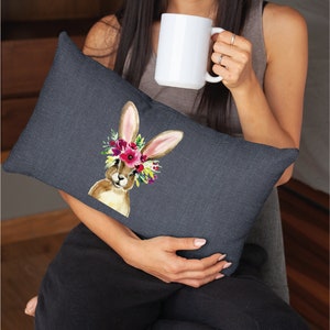 May include: A dark gray throw pillow with a watercolor illustration of a brown bunny wearing a floral crown. The bunny is looking directly at the viewer.