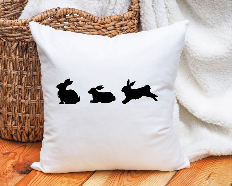 May include: White throw pillow with three black bunny silhouettes. The bunnies are in a line, with the first bunny sitting, the second bunny sitting, and the third bunny hopping.