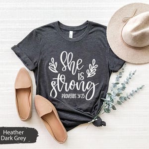 May include: Heather dark grey t-shirt with the text "She is strong Proverbs 31:25" in white lettering.