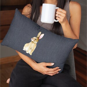 May include: A dark grey throw pillow featuring a watercolour illustration of a brown rabbit with long ears. The rabbit is looking to the left.