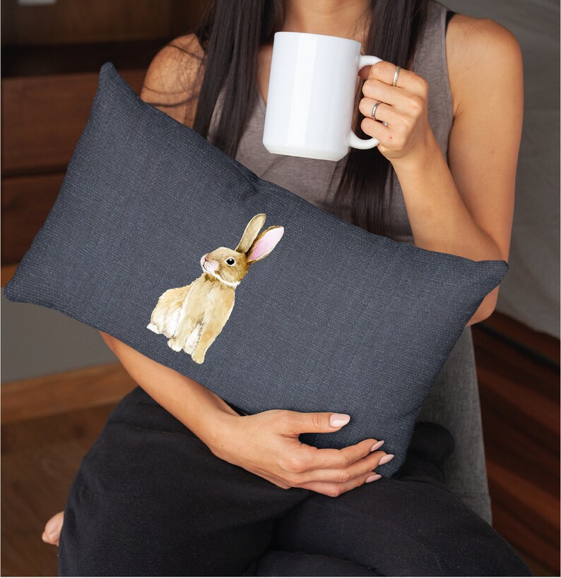 May include: A dark grey throw pillow featuring a watercolour illustration of a brown rabbit with long ears. The rabbit is looking to the left.