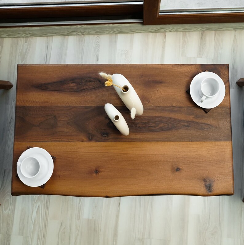 Op de afbeelding: Een houten salontafel met een natuurlijke houten afwerking. De tafel heeft een natuurlijke rand en is versierd met drie witte keramische vazen en een witte keramische kop en schotel.