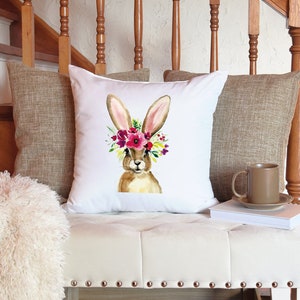 May include: White throw pillow with a watercolor illustration of a brown bunny wearing a pink, red, and yellow flower crown.
