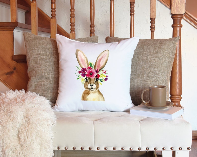 May include: White throw pillow with a watercolor illustration of a brown bunny wearing a pink, red, and yellow flower crown.