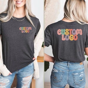 May include: A dark heather grey t-shirt with a custom logo printed on the front and back. The logo is in a retro style with colorful letters that spell out "CUSTOM LOGO".