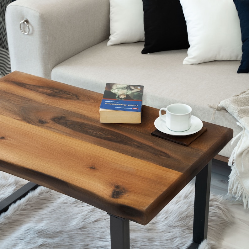 Op de afbeelding: Een houten salontafel met een live edge blad en zwarte metalen poten. Een boek getiteld "Civil Disobedience" van Henry David Thoreau ligt op de tafel, samen met een witte koffiekop en een schoteltje.
