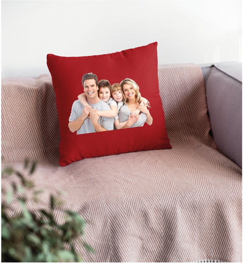 May include: Red throw pillow with a printed image of a family of four smiling and hugging. The pillow is on a couch with a brown and white patterned throw.