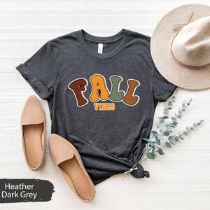 May include: A dark heather grey t-shirt with the text "Fall Vibes" in colourful, retro-style lettering.