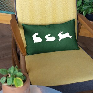 May include: A green throw pillow with white bunny silhouettes on a yellow chair.
