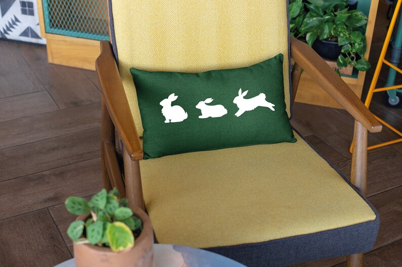 May include: A green throw pillow with white bunny silhouettes on a yellow chair.