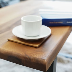 Op de afbeelding: Een witte keramische koffiekop en schotel op een houten tafel met een blauw boek op de achtergrond.