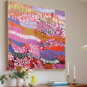 May include: Abstract art print in a gold frame. The artwork features a colorful composition of pink, red, blue, yellow, and white shapes. The painting hangs above a wooden cabinet with candles and a vase of flowers.
