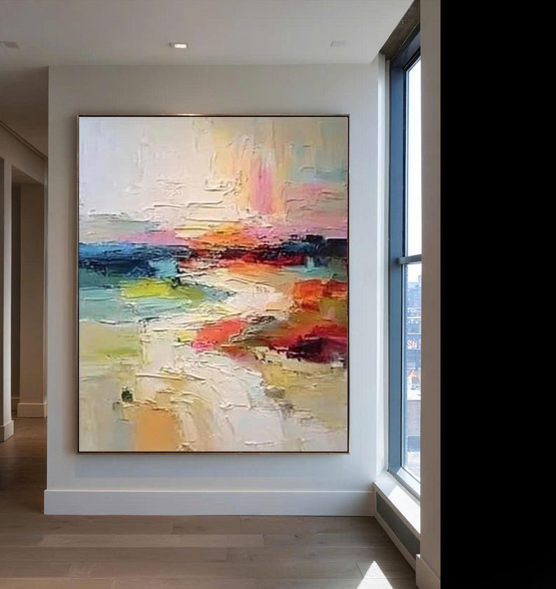 May include: Large abstract painting with a textured surface. The artwork features a landscape with a palette of colors including white, pink, orange, blue, green, and red. The painting is framed and displayed on a white wall.