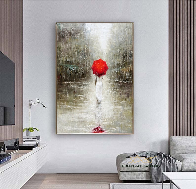 May include: A painting of a woman walking in the rain with a red umbrella. The painting is done in a muted palette of grays and browns, with a touch of red from the umbrella. The woman is wearing a white dress and is walking away from the viewer. The painting is set in a city street, with buildings and trees visible in the background.