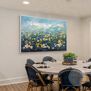 K&ouml;nnte beinhalten: Ein Gem&auml;lde, das ein Feld mit wei&szlig;en und gelben Blumen vor einem blauen Himmel mit wei&szlig;en Wolken zeigt. Das Gem&auml;lde ist in einem wei&szlig;en Rahmen gerahmt und h&auml;ngt an einer Wand in einem Esszimmer. Das Esszimmer hat einen runden Tisch mit St&uuml;hlen und eine Pflanze auf einem Tisch.