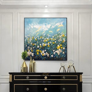 K&ouml;nnte beinhalten: Eine schwarze Kommode mit goldenen Verzierungen und drei Schubladen. Die Kommode ist mit einem Gem&auml;lde eines Feldes mit gelben und wei&szlig;en Blumen vor blauem Himmel dekoriert. Auf der Kommode stehen zwei Glasskulpturen.