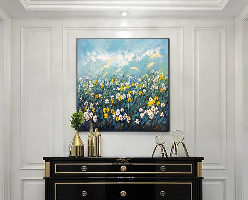 K&ouml;nnte beinhalten: Eine schwarze Kommode mit goldenen Verzierungen und drei Schubladen. Die Kommode ist mit einem Gem&auml;lde eines Feldes mit gelben und wei&szlig;en Blumen vor blauem Himmel dekoriert. Auf der Kommode stehen zwei Glasskulpturen.