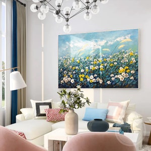 K&ouml;nnte beinhalten: Ein Gem&auml;lde, das ein Feld mit wei&szlig;en und gelben Blumen zeigt, mit einem blauen Himmel und wei&szlig;en Wolken im Hintergrund. Das Gem&auml;lde h&auml;ngt an einer wei&szlig;en Wand in einem Wohnzimmer.