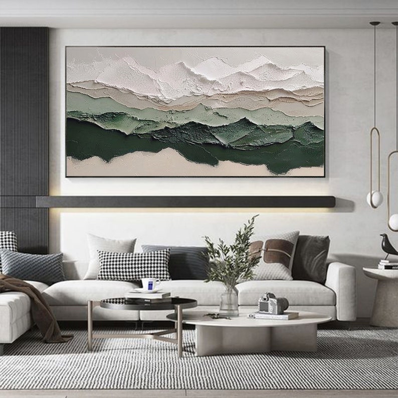 May include: Abstract landscape painting with white, beige, and green colors. The painting is framed and hanging on a wall in a living room setting.