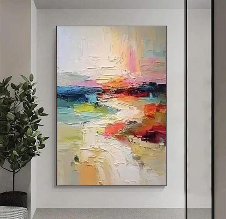 May include: Abstract landscape painting with thick brushstrokes. The artwork features a vibrant color palette of blues, greens, oranges, and pinks, creating a textured and dynamic composition. The painting is framed and mounted on a wall.